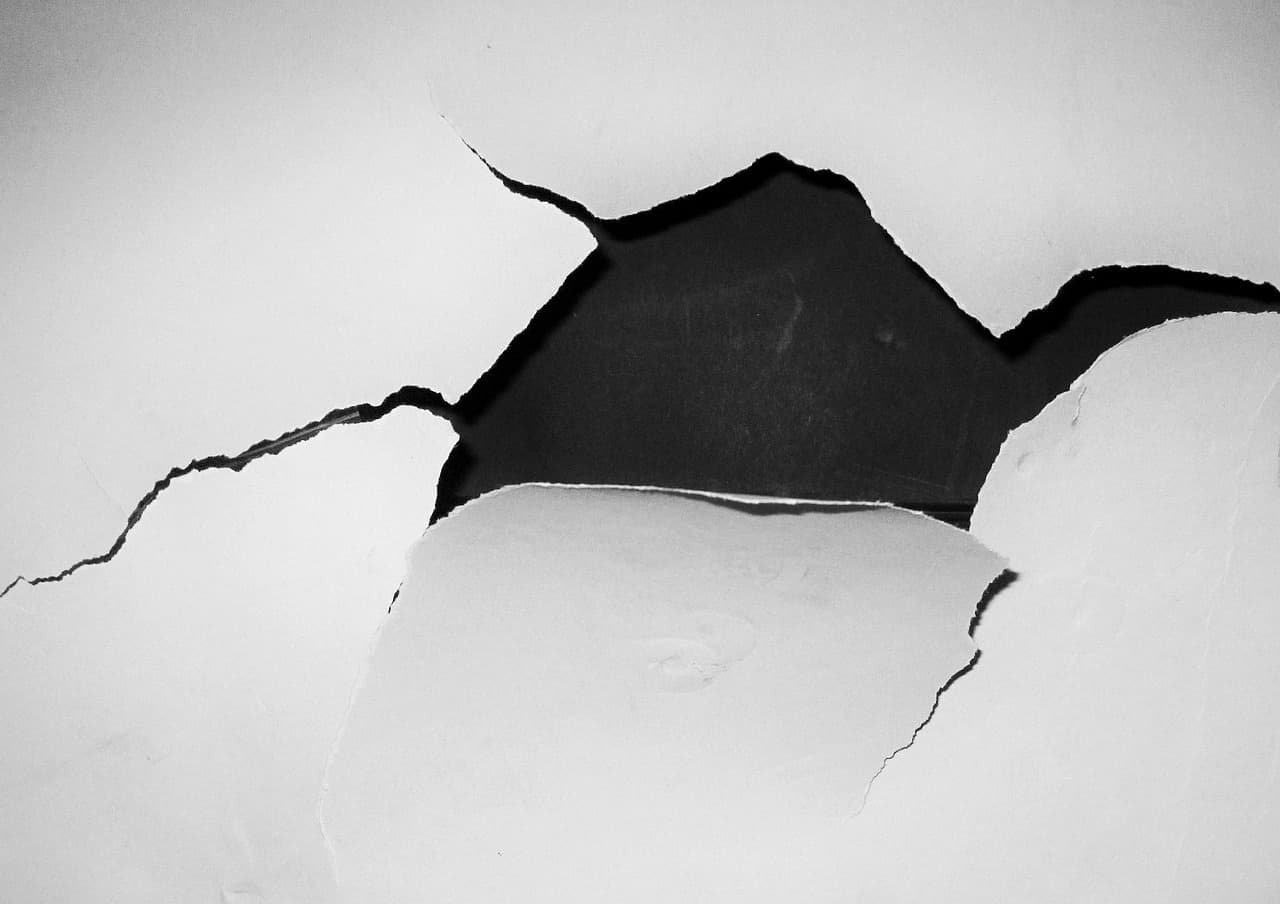 Hole and cracks in a white plaster wall
