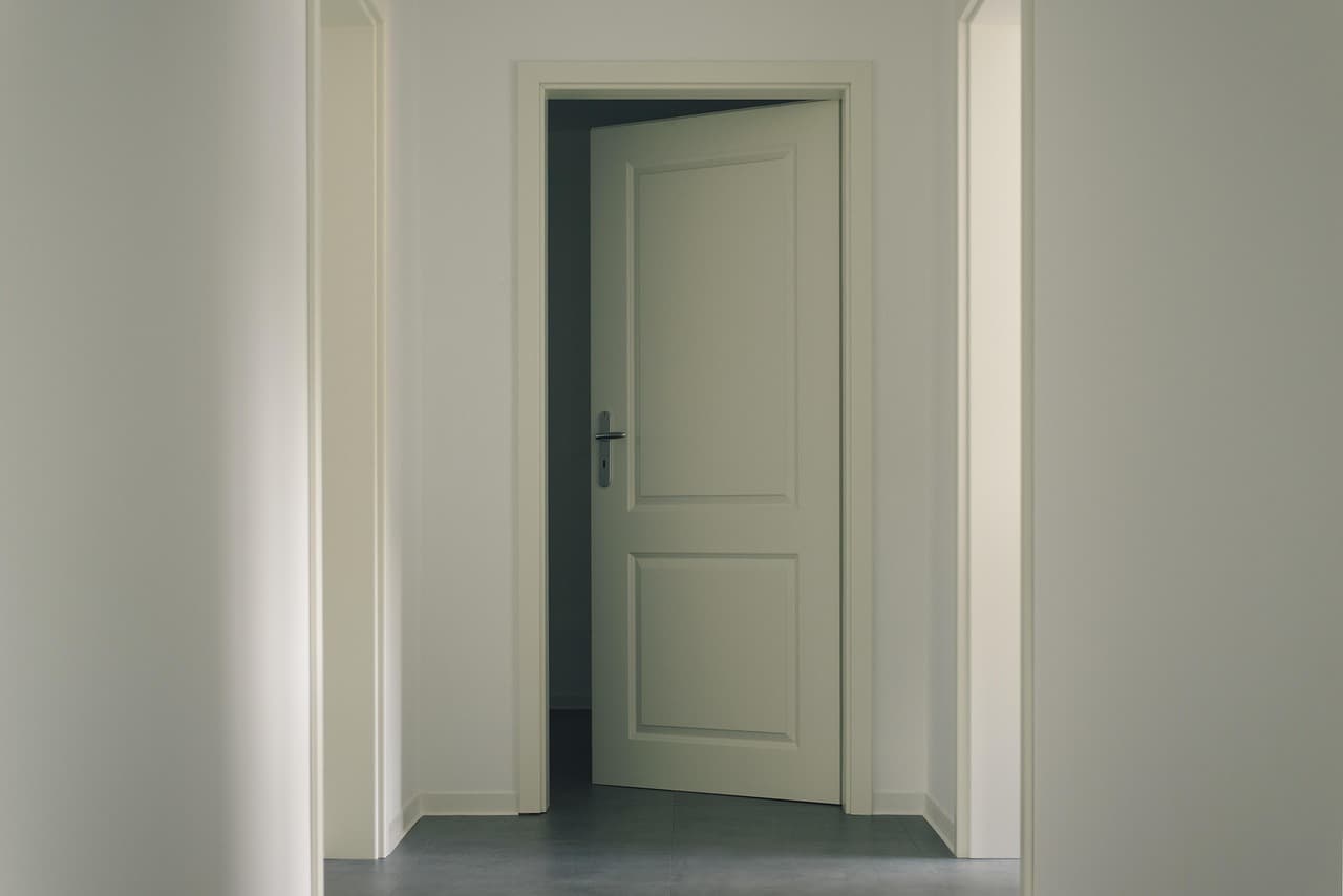 Plain white hallway wall with a panelled door ajar